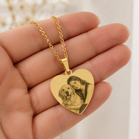 Collana personalizzata con ciondolo a cuore in acciaio dorato tenuta nel palmo di una mano per mostrare le dimensioni reali dell'incisione fotografica